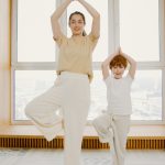 Une femme jeune et un enfant en train de faire la posture de l'arbre en yoga